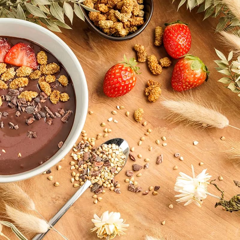 Schokoladen-Bowl mit Erdbeeren, Maulbeeren und Kakaonibs auf Holz, Food-Aufnahme von oben