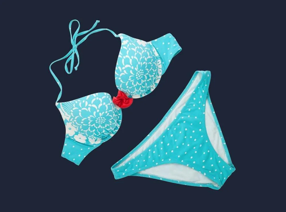 Türkiser Bikini mit Blumenmuster, Oberteil und Hose flach gelegt, freigestellt vor dunkelblauem Grund