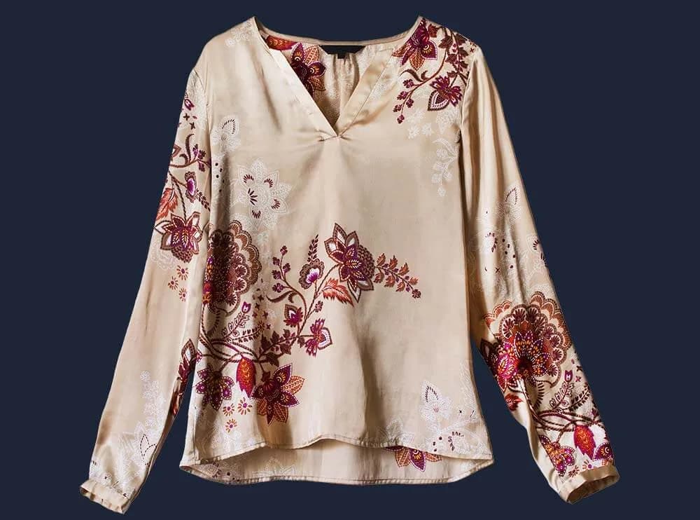 Beige Bluse mit roten Blumenranken als Hollowman-Aufnahme, freigestellt vor dunkelblauem Grund