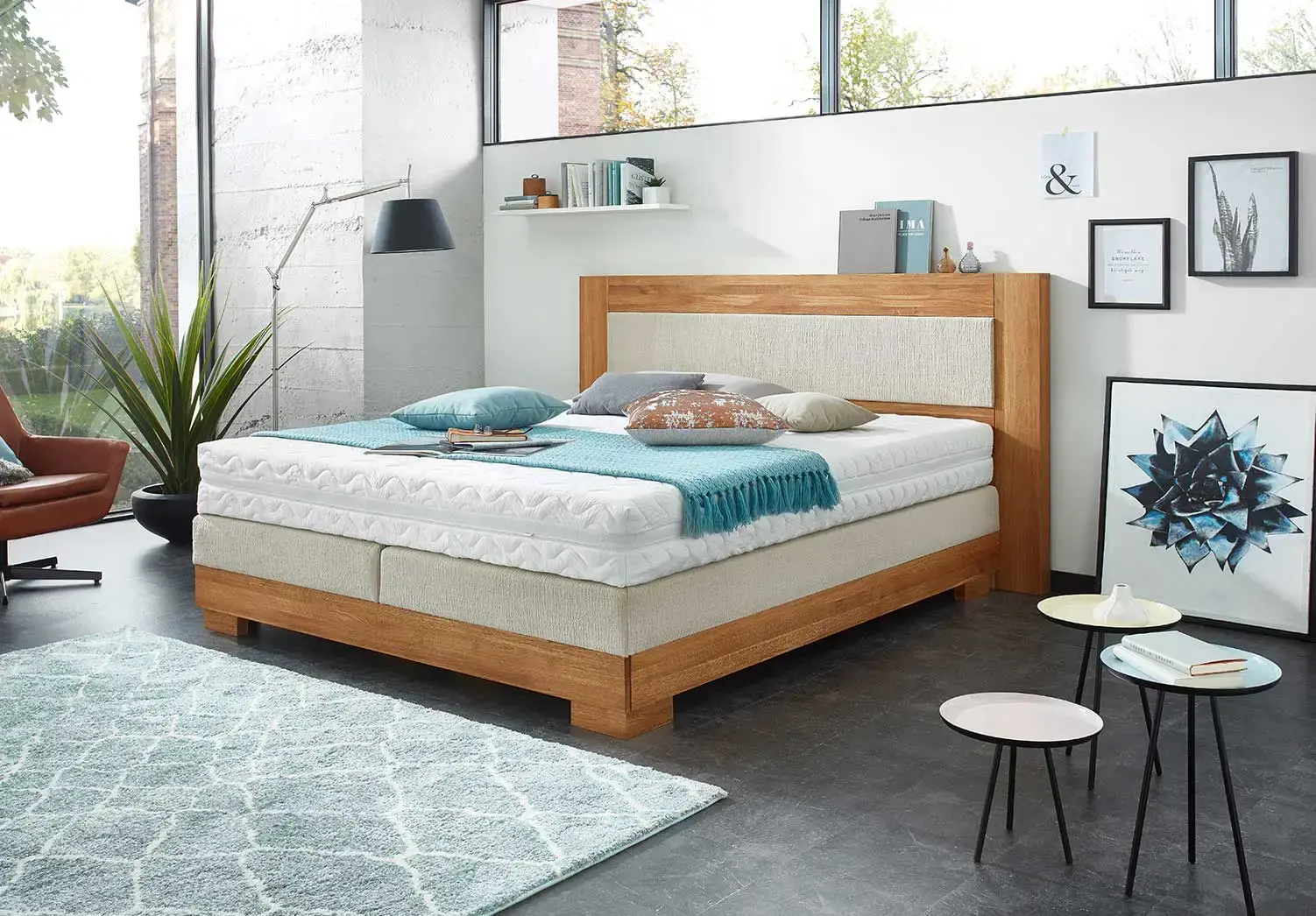 Boxspringbett mit türkiser Bettwäsche in einem hellen Schlafzimmer mit Teppich und Beistelltischen, 3D-Visualisierung