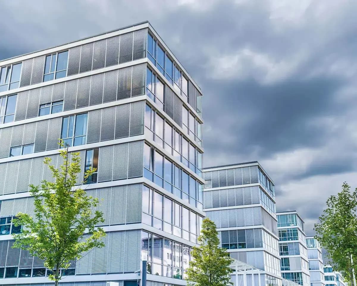 Bürogebäude mit Glasfassade unter grauem Wolkenhimmel, Ausgangsbild vor dem Himmelstausch