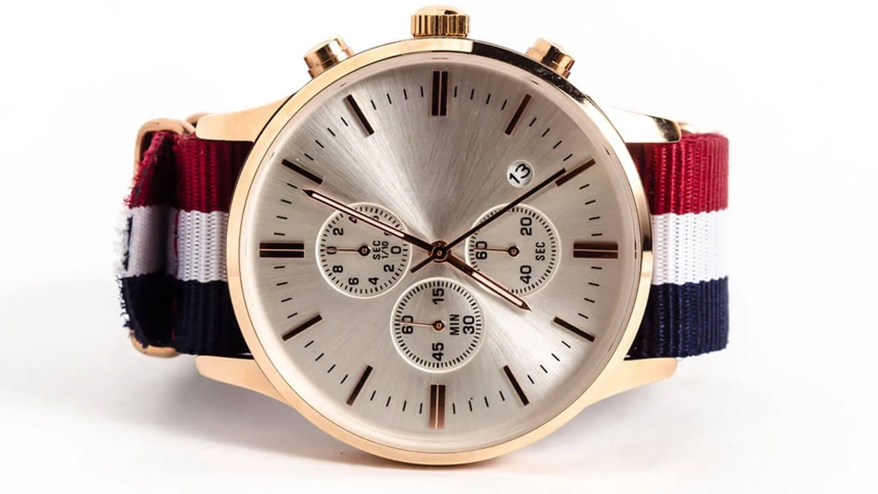Chronograph mit roségoldfarbenem Gehäuse, hellem Zifferblatt und gestreiftem Textilband vor Weiß