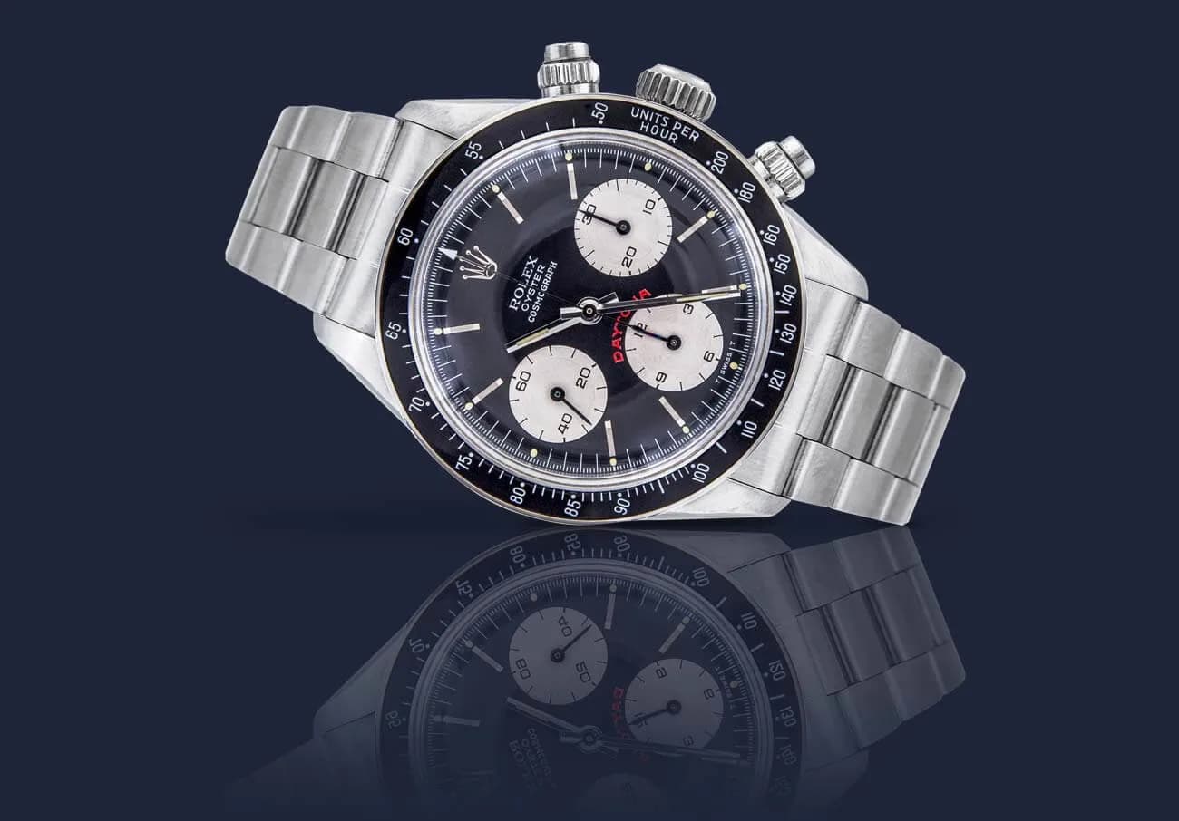 Chronograph mit Metallarmband und schwarzem Zifferblatt vor dunkelblauem Grund mit Spiegelung am Boden