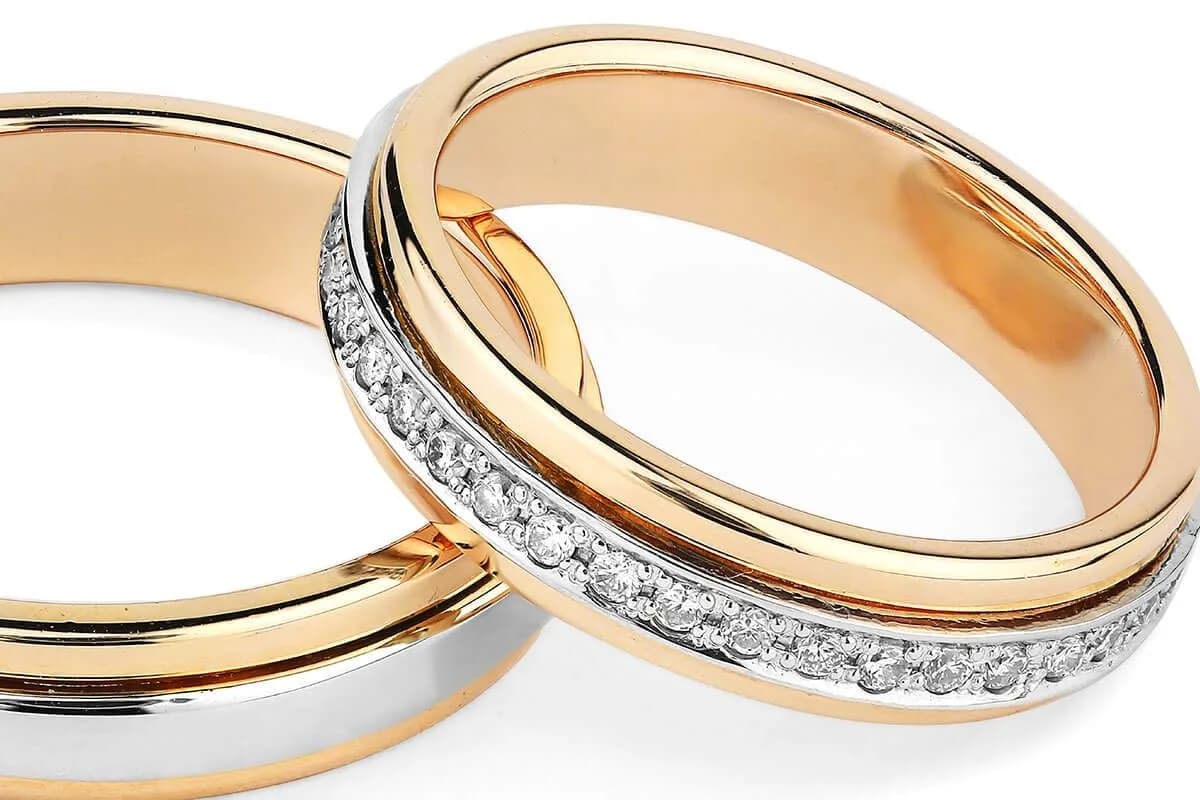 Nahaufnahme zweier Eheringe in Gelb- und Weißgold, die Steinreihe im Weißgoldband ist scharf gezeichnet
