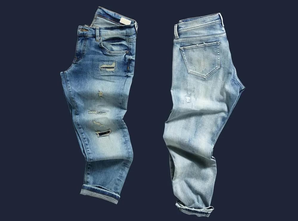 Zwei Jeans im Used-Look, flach gelegt und freigestellt vor dunkelblauem Grund