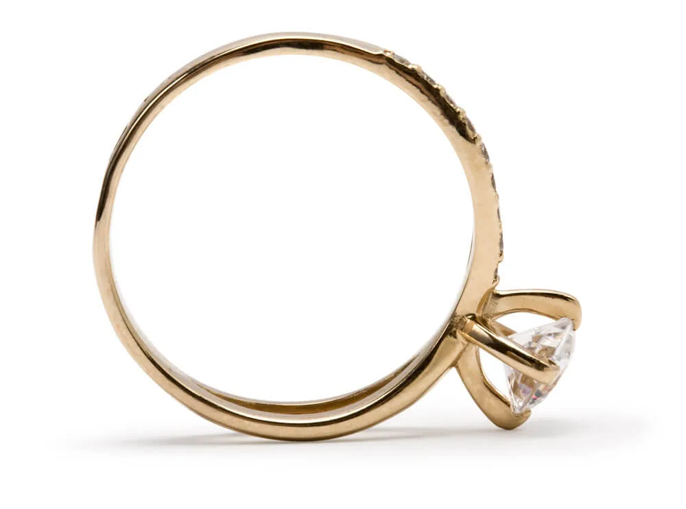 Goldener Solitärring mit klarem Stein in der Seitenansicht, stehend vor Weiß mit feinem Schatten
