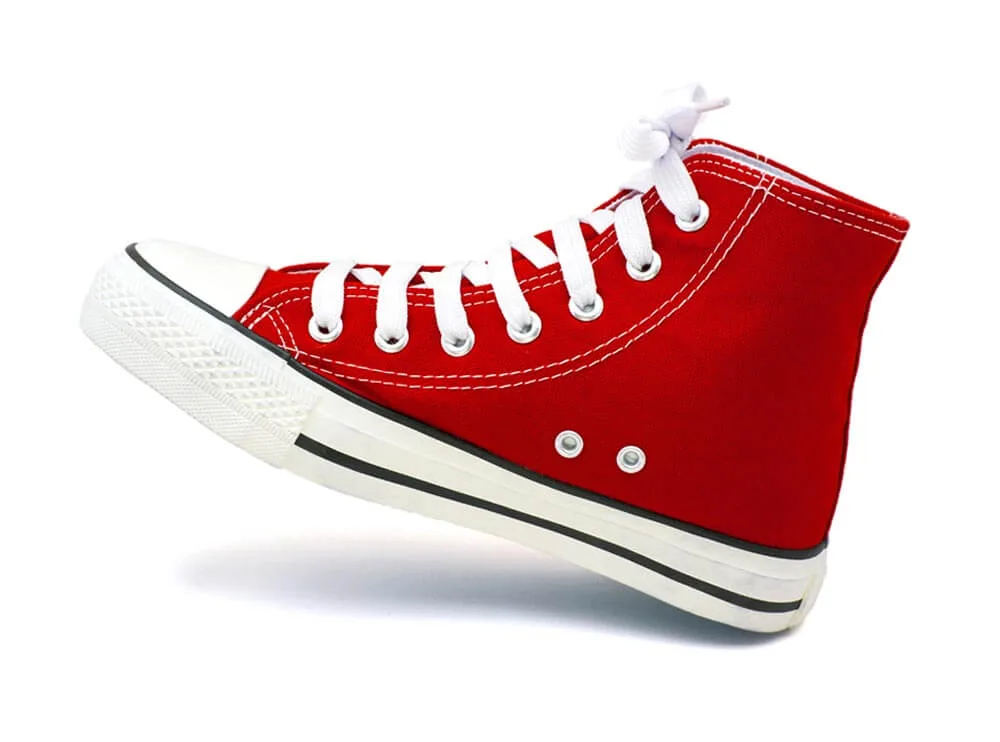 Roter Stoffturnschuh mit weißer Sohle und Schnürsenkeln, schwebend freigestellt mit Schatten