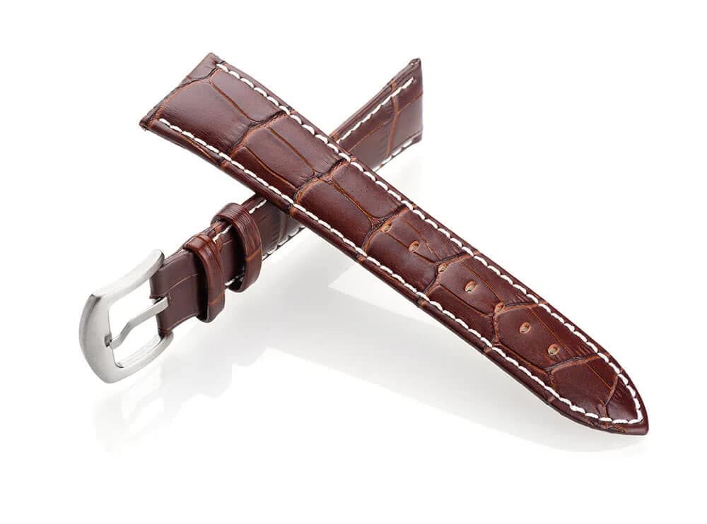 Braunes Uhrenarmband aus Leder mit Kroko-Prägung und Dornschließe, gekreuzt freigestellt vor Weiß