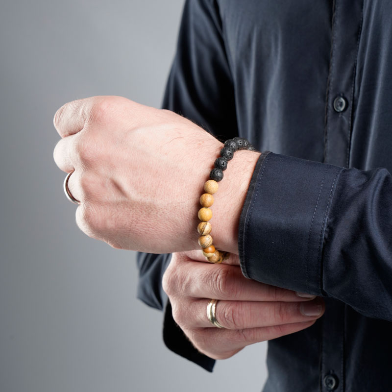 Professionelle Schmuck-fotografie einer braun-schwarzen Holzkette für das Handgelenk und Ringe für die Finger, angelegt an die Hände eines Mannes.