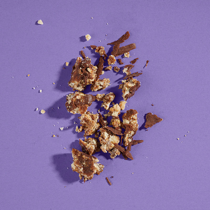Professionelle Mood-Fotografie einer zerstückelten Schokolade vor lila Hintergrund