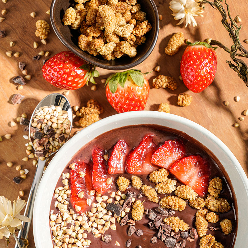 Professionelle Lifestyle- und Mood-Fotografie einer Schoko-Fitness bowl gefüllt mit Erdbeeren,Müsli und ansprechender Dekoration aus Erdbeeren und Zerealien.