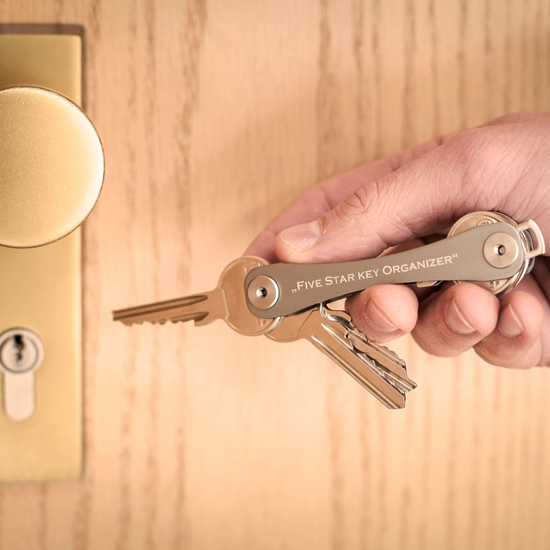 Professionelle Lifestyle-Fotografie eines Schlüsselbunds von "Five star key organizer" in einer männlichen Hand kurz vor dem Schlüsselloch einer Tür.
